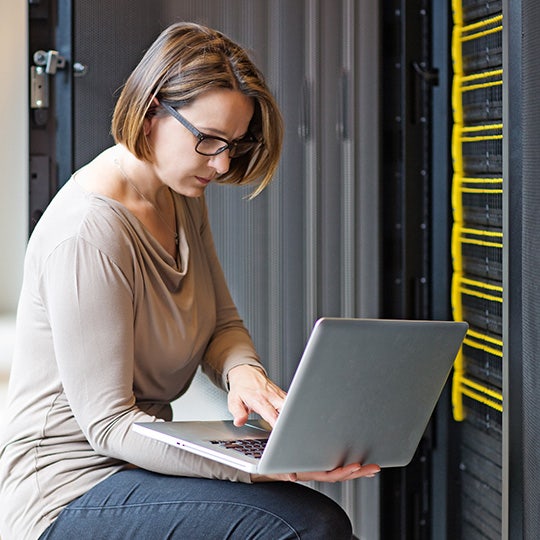 vrouw werkt op een laptop in een serverruimte