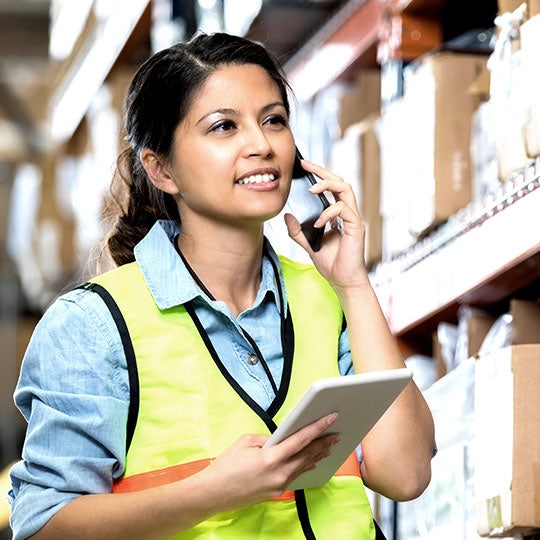 medewerker in een magazijn belt met een smartphone en heeft een tablet vast