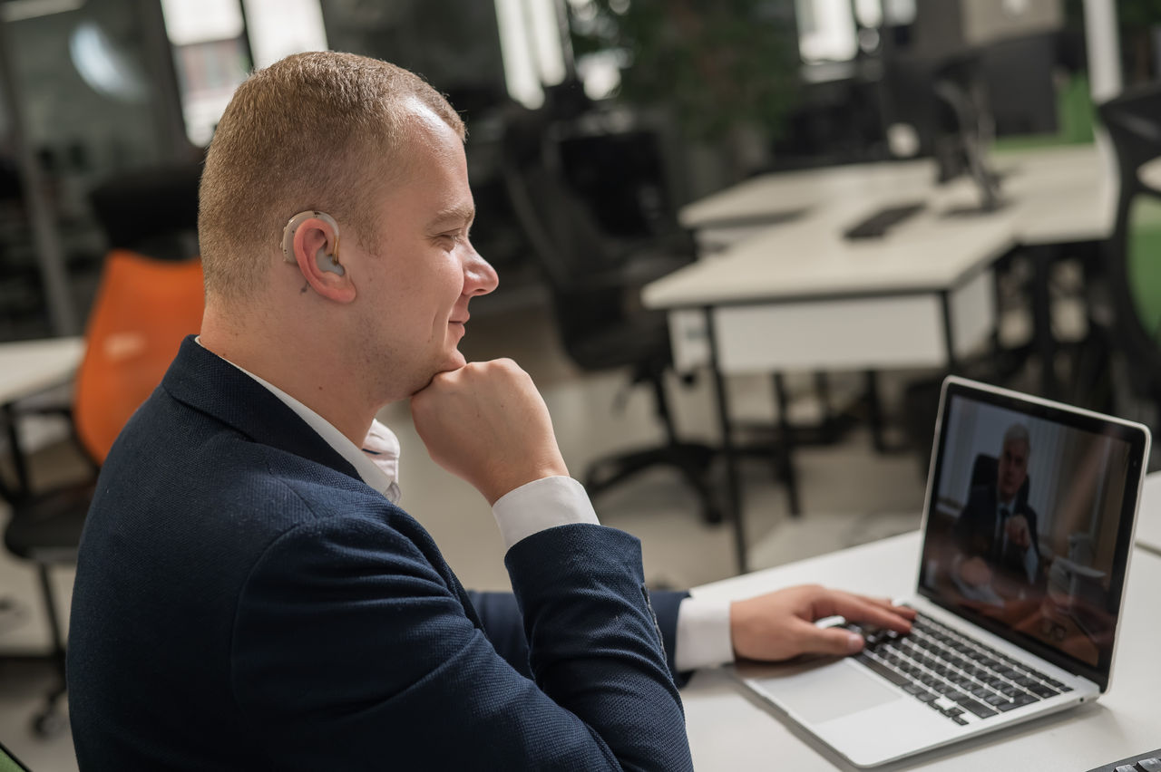 Caucasian man with hearing aid at online meeting on laptop